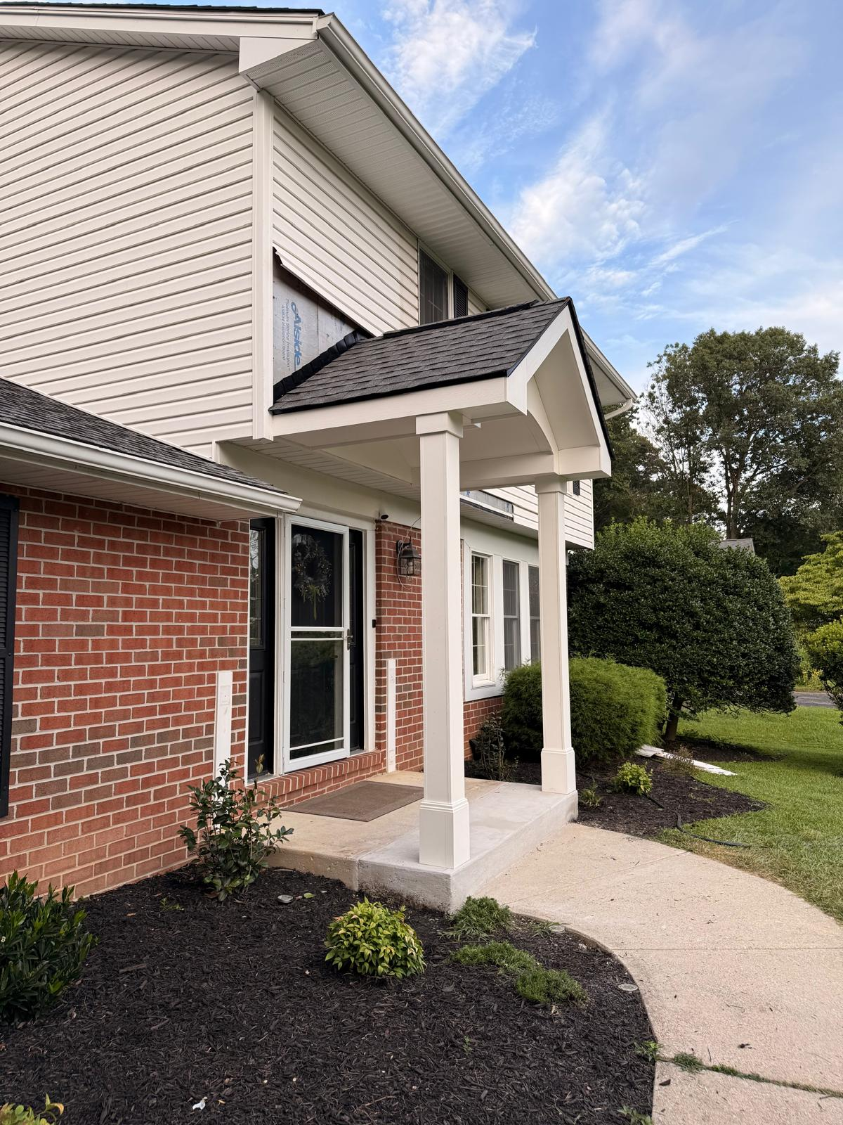 Finished front portico with shingled gable roof, white columns, and new landscaping